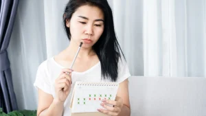 A woman checks her calendar, concerned about her irregular periods and considering seeking treatment.
