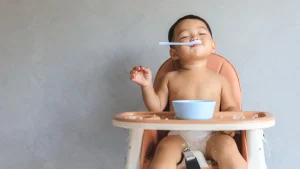 A happy baby enjoys their first taste of solid food, an important milestone in baby health and child nutrition.